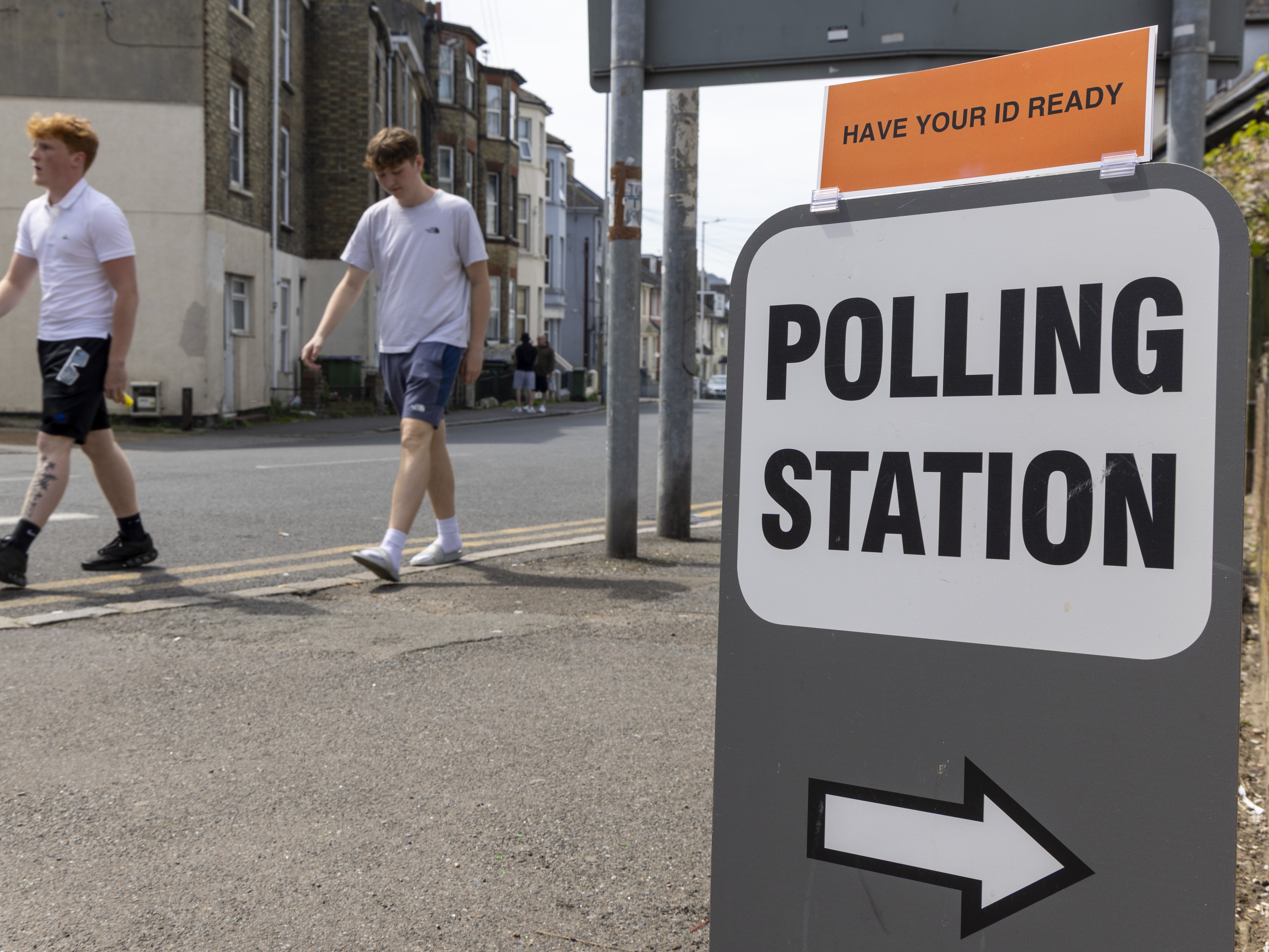 caption: People walk past a sign for a polling station during local council elections in Folkestone, England in May. The British government is announcing plans to lower the voting age to 16.