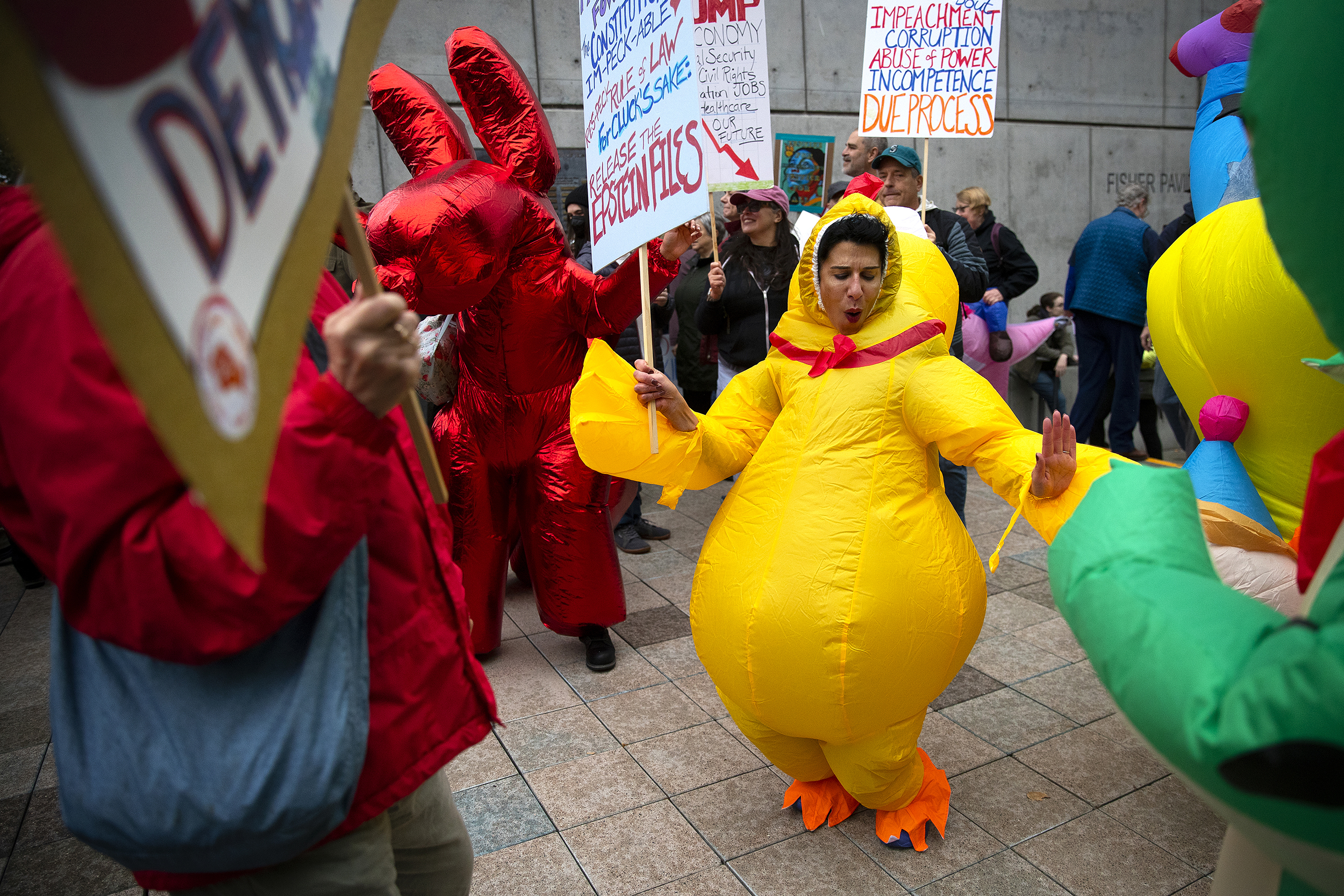 caption: Protesters, including Amina Suchoski, center, dance and laugh while dressed in inflatable costumes during the second No Kings rally on Saturday, October 18, 2025, at Seattle Center. "Trump is trying to divide, distract, and dominate us," said protest organizer Kathleen Carson of Seattle Indivisible. "We know this playbook — dictators divide to conquer. We unite to resist."