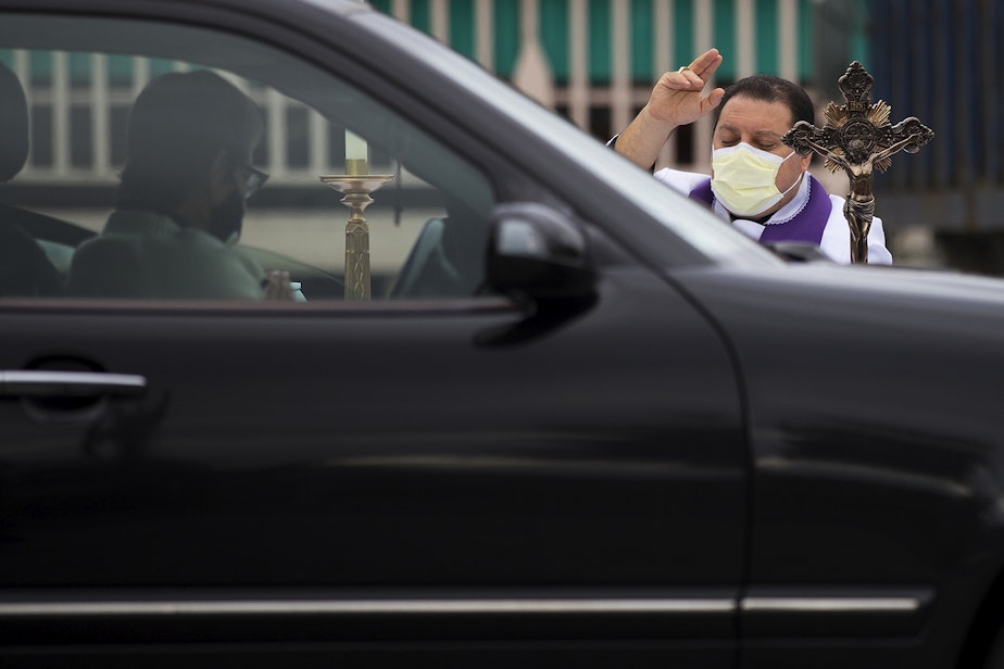 caption: Father Jose Alvarez, right, during walk and drive through confessions on Friday, April 24, 2020, in the parking lot at Holy Family Roman Catholic Church in White Center. 