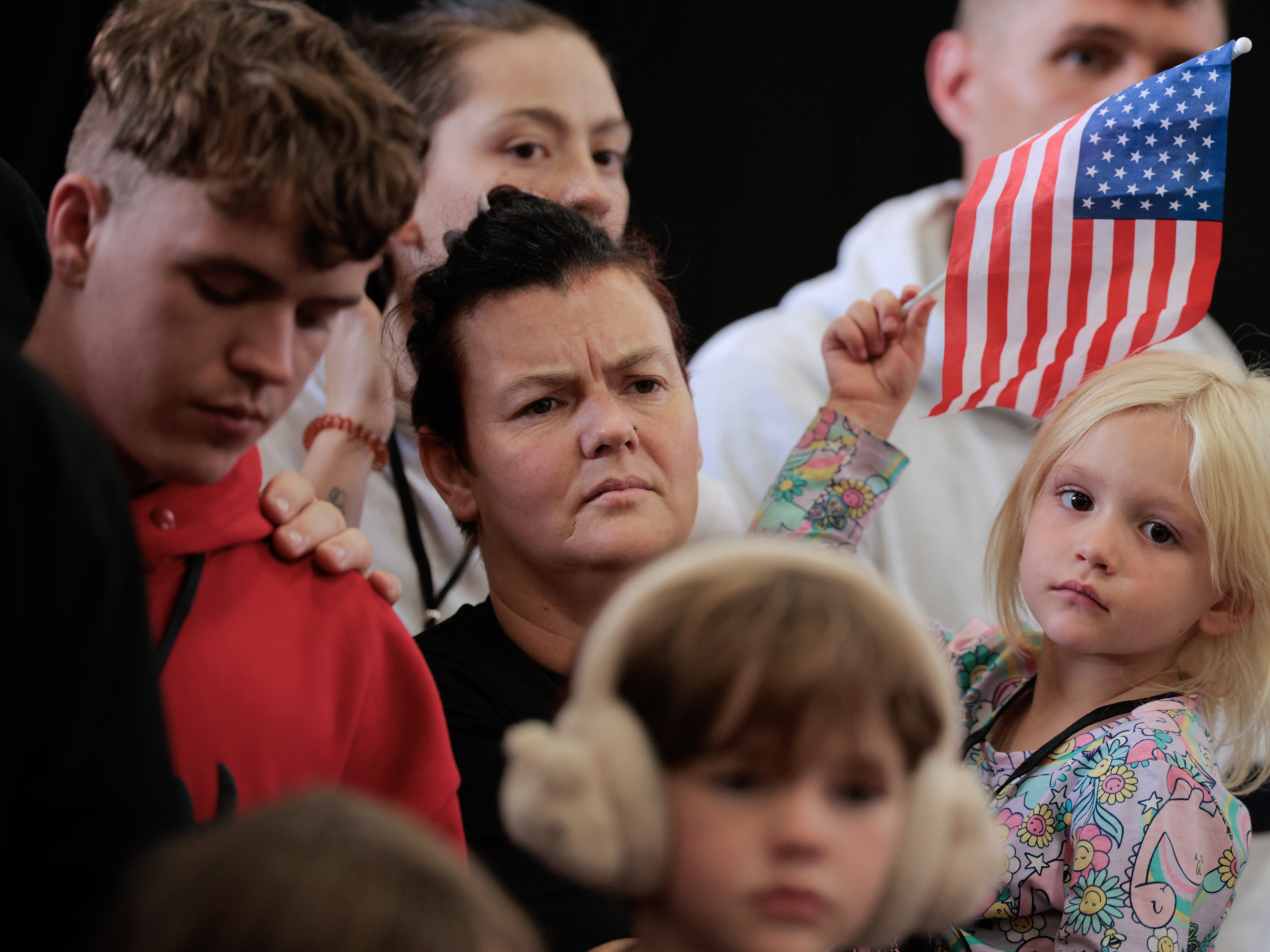 caption: Newly arrived South Africans listen to representatives from Homeland Security and the State Department deliver welcome statements in a hangar at Atlantic Aviation Dulles near Washington Dulles International Airport on May 12, 2025 in Dulles, Va.