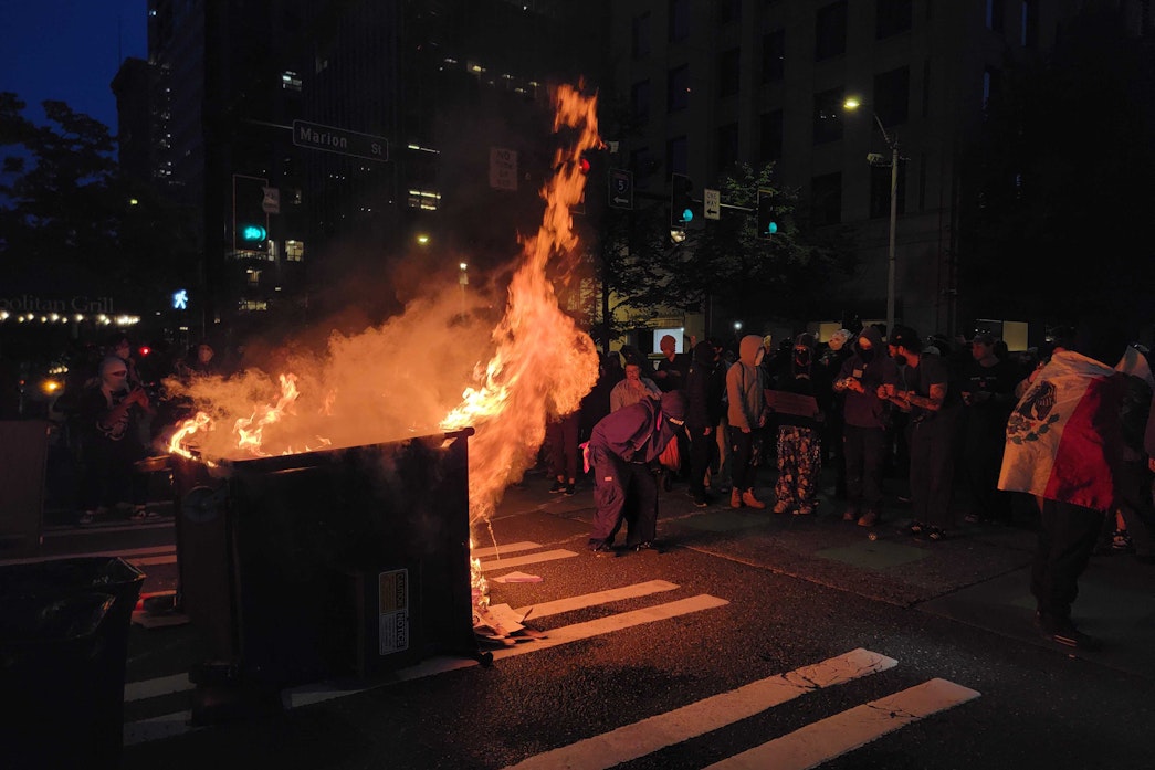 caption: A dumpster burns during a protest in downtown Seattle on June 11, 2025.