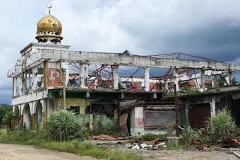 caption: The skeletal remains of a mosque stand amid overgrown shrubs. Authorities say 25 mosques were destroyed in the district most affected by the five months of fighting between government forces and ISIS militants in Marawi.