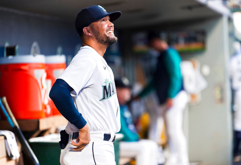 caption: Seattle Mariners first base coach Kristopher Negron smiles in the dugout as the team warms up before a baseball game against the Texas Rangers, Wednesday, Sept. 28, 2022, in Seattle. The Mariners won 3-1. 