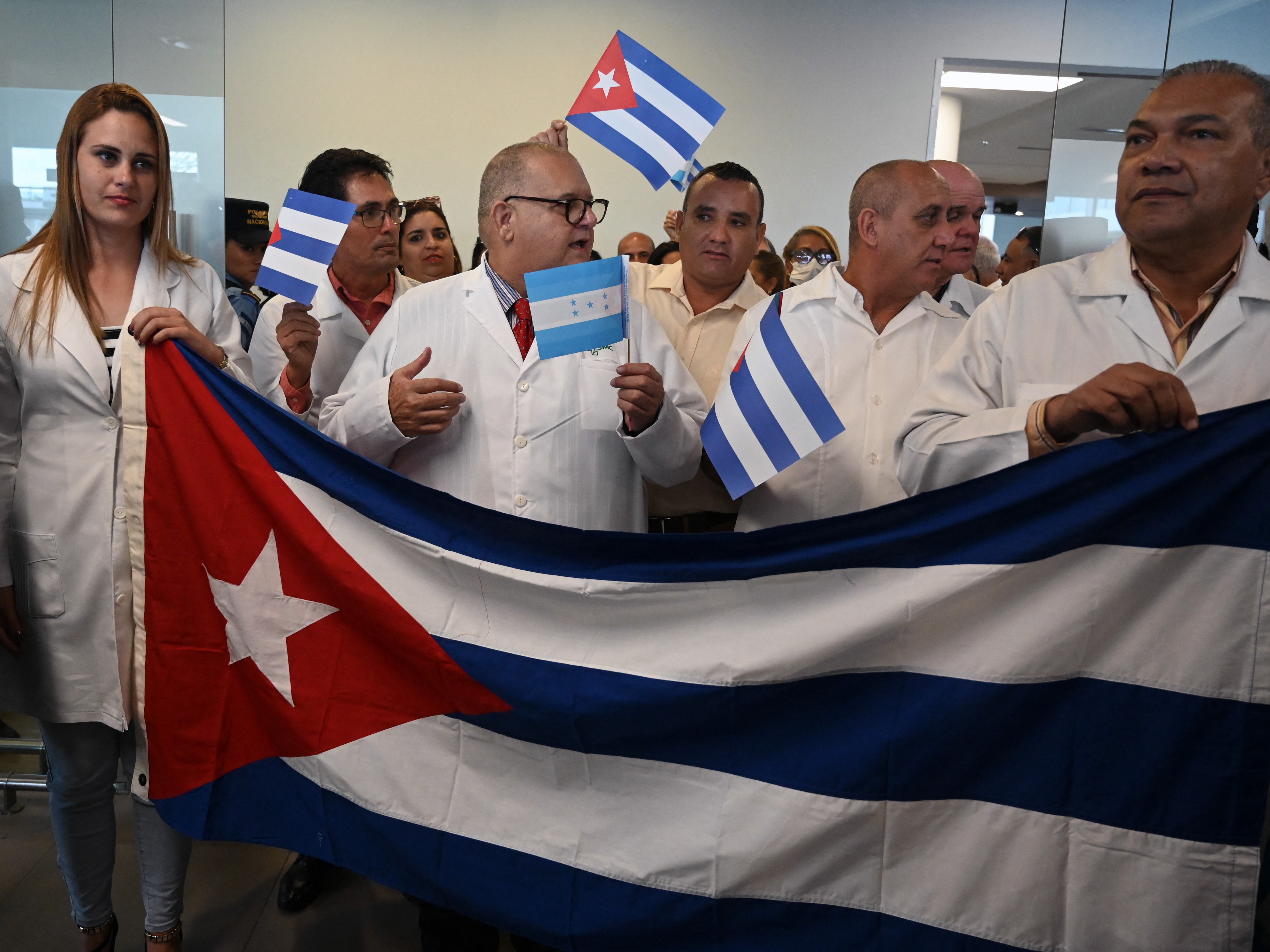 caption: Cuban doctors hold their national flag upon arriving in Honduras for a medical mission in February 2024. Now the doctors are leaving Honduras as the U.S. urges countries to reconsider their agreements with Cuba.