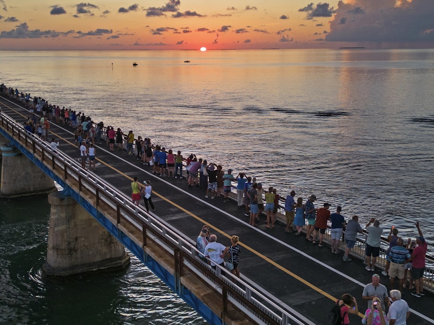 caption: In this aerial photo provided by the Florida Keys News Bureau, attendees watch and toast the sunset at a Florida Keys bicentennial celebration, Friday, May 19, 2023, on the restored Old Seven Mile Bridge in Marathon, Fla.