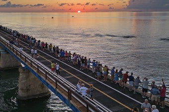 caption: In this aerial photo provided by the Florida Keys News Bureau, attendees watch and toast the sunset at a Florida Keys bicentennial celebration, Friday, May 19, 2023, on the restored Old Seven Mile Bridge in Marathon, Fla.