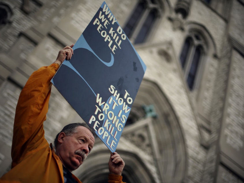 caption: Death penalty opponent Herve Deschamps holds a sign during a vigil outside St. Francis Xavier College Church in St. Louis, hours before 2014 scheduled execution of death row inmate Russell Bucklew.