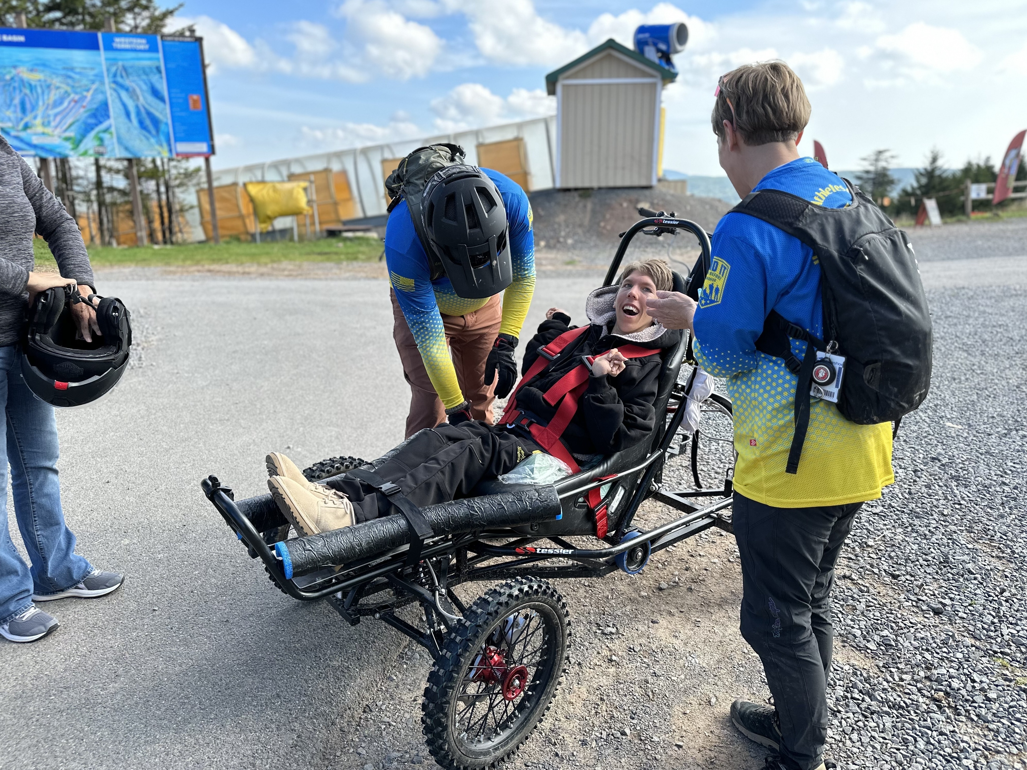 caption: Before heading out on the trail, Carol Woody and volunteer Erwin Berry make sure Gage Tatar is safely buckled into the Cimgo. Grinning wide, Tatar listens as Woody explains what he can expect on the dirt track.