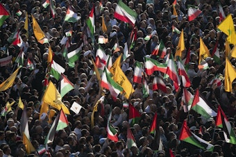 caption: People carry Palestinian flags, Iranian flags and Hezbollah flags at Tehran's Revolution Square during an anti-Israel rally on Oct. 18.