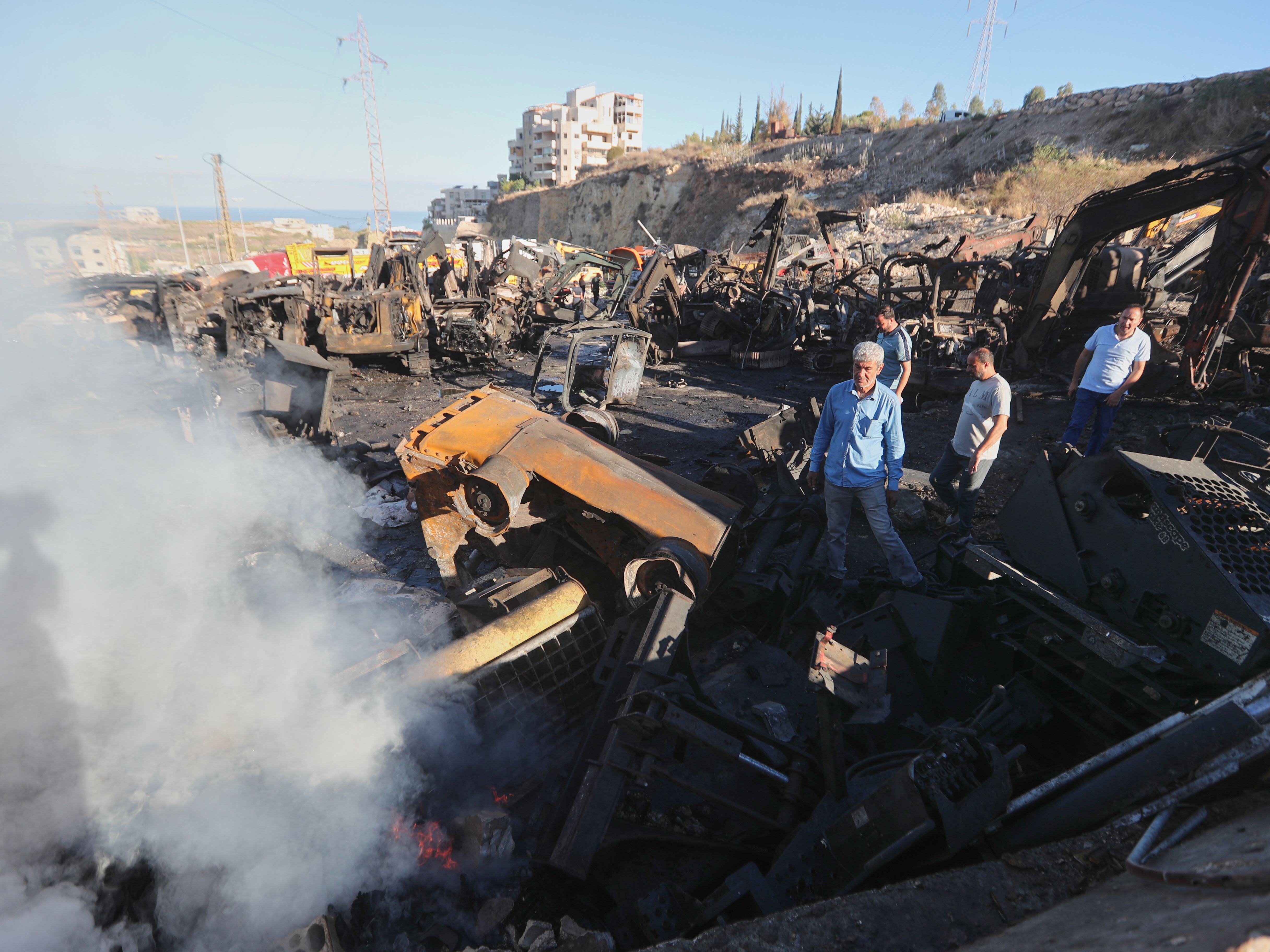 caption: People gather at a site that sold heavy machinery, where a large number of vehicles were destroyed in Israeli airstrikes, in the southern village of Msayleh, Lebanon, Saturday, Oct. 11, 2025.
