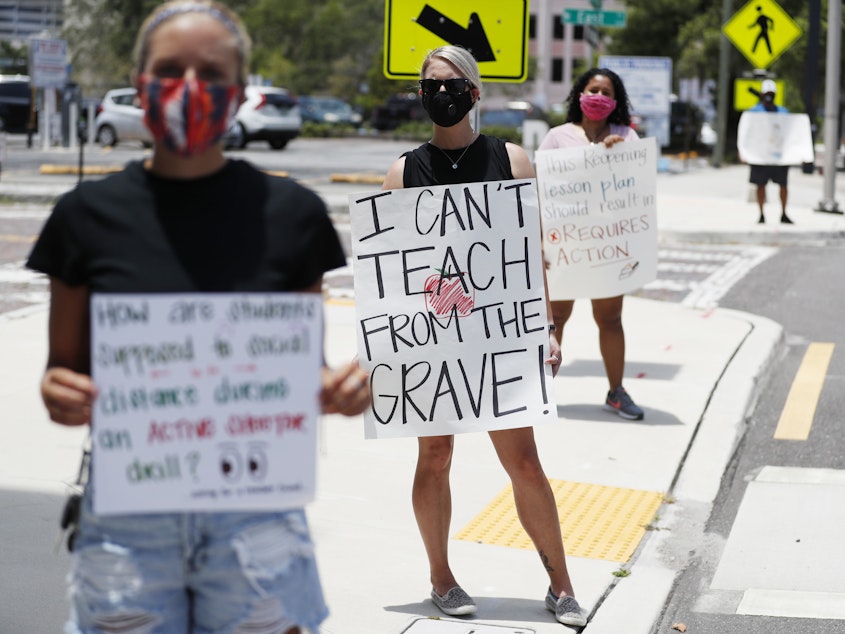 caption: Middle school teacher Brittany Myers, (C) stands in protest at the Hillsborough County Schools District Office on Thursday in Tampa, Fla. Teachers and administrators rallied against the reopening of schools due to health and safety concerns amid the COVID-19 pandemic.