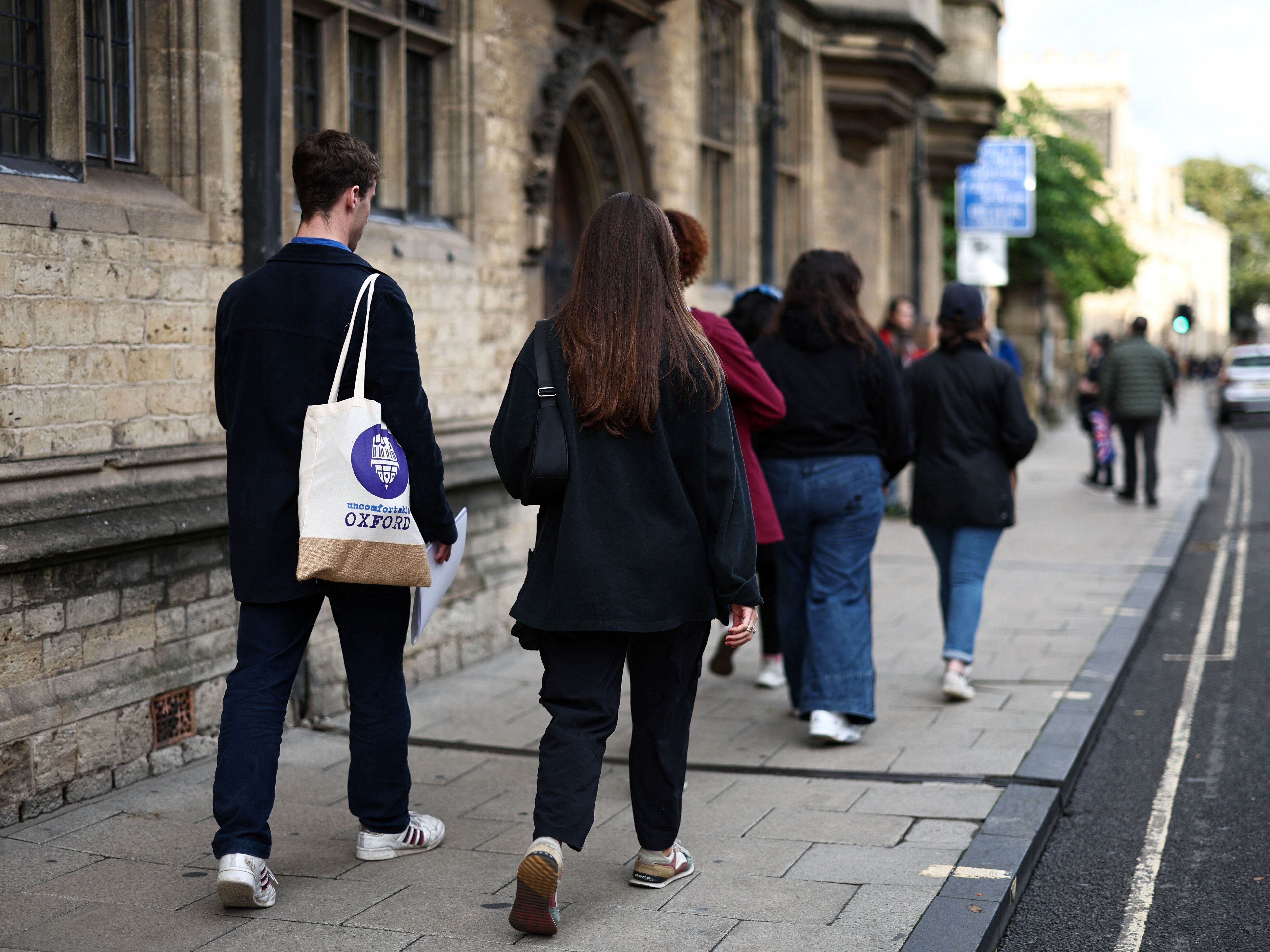 caption: A tour guide walks with a group of people attending an Uncomfortable Oxford Tour, in Oxford, on Oct. 20, 2023.