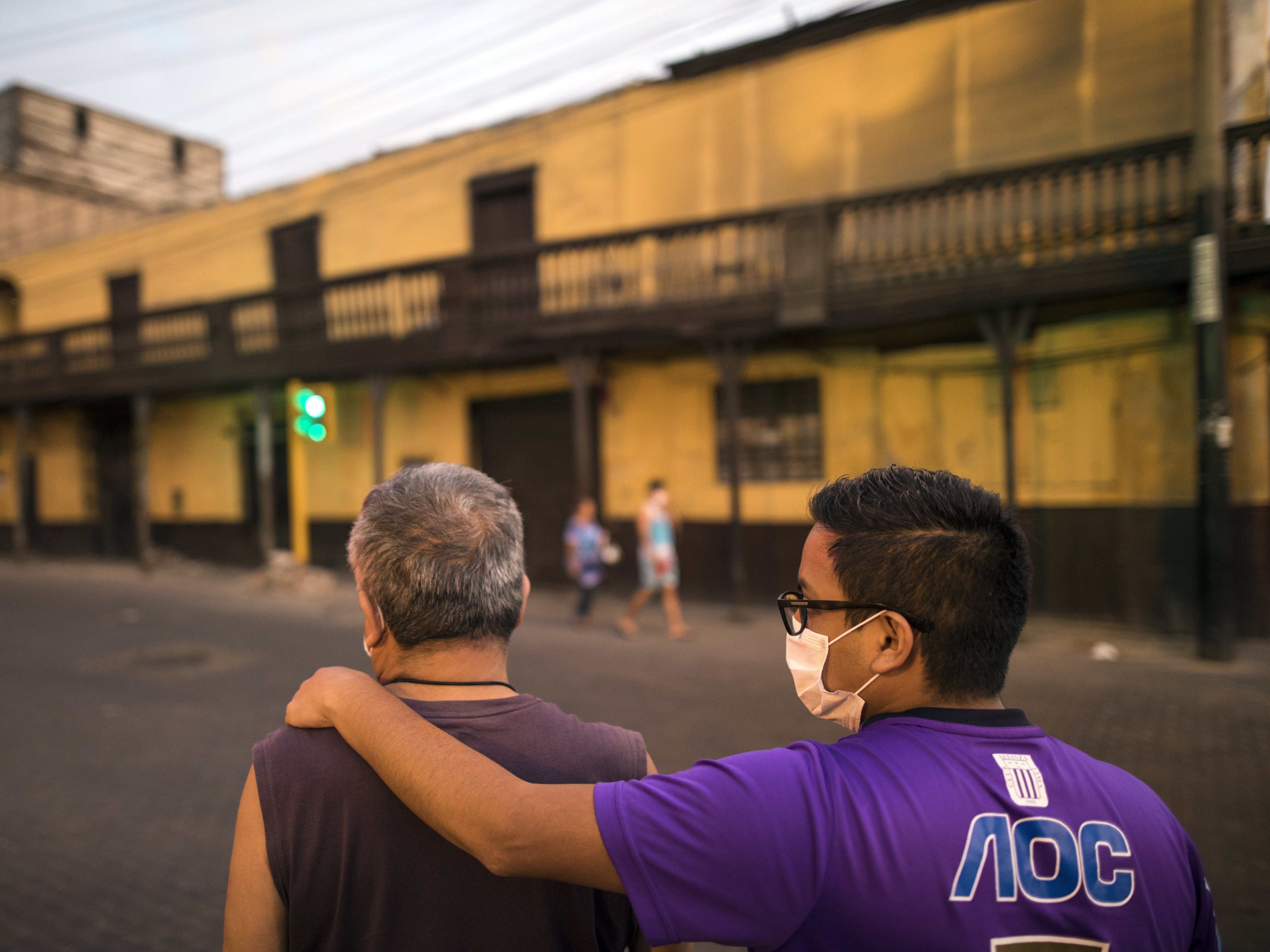 caption: A pair of men wearing masks — but neglecting social distancing guidelines — wait for public transportation in Peru's capital, Lima. The country recently urged men and women to leave their homes only on separate days, in an attempt to slow the spread of the coronavirus.
