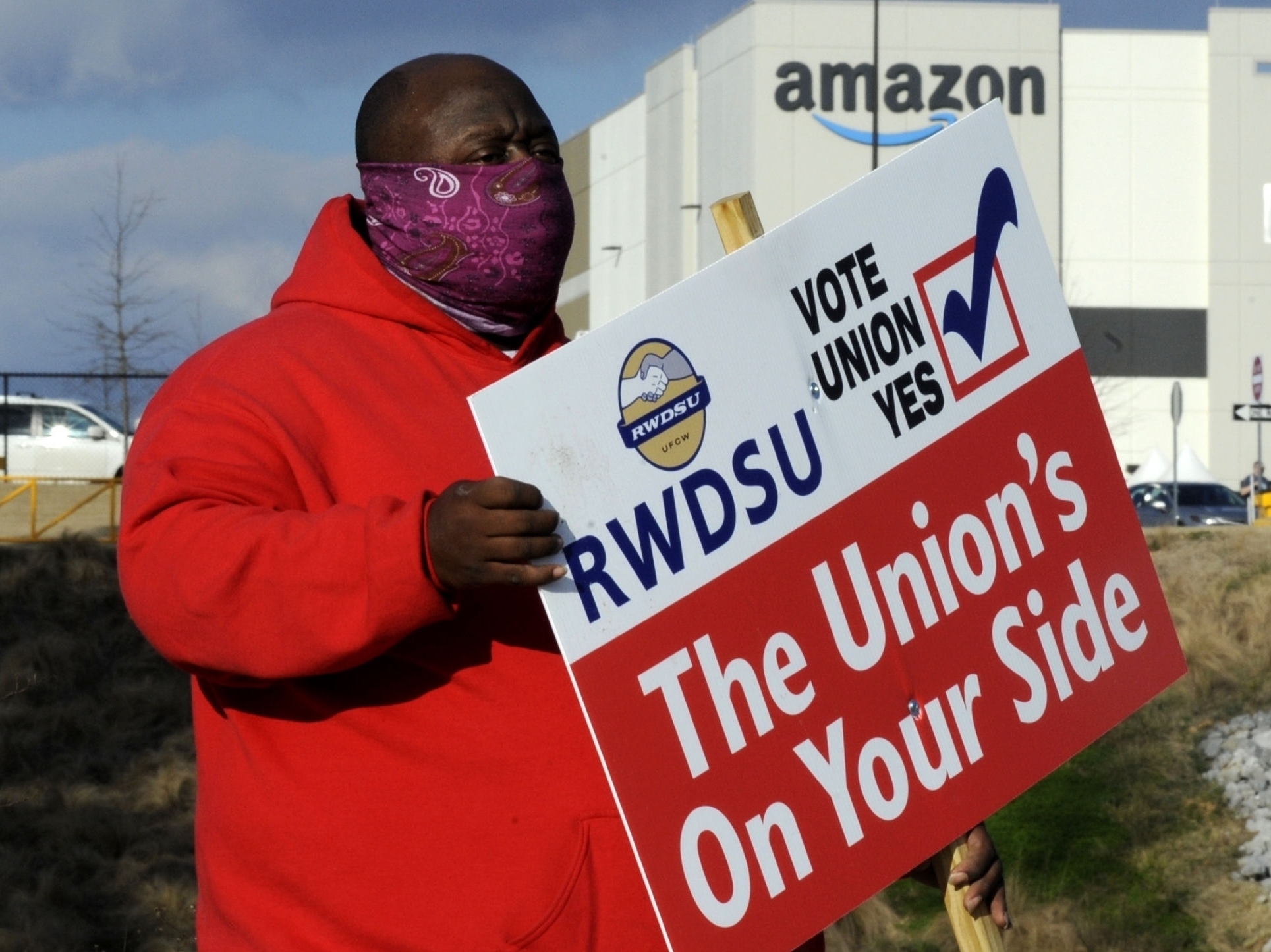 caption: Michael Foster of the Retail, Wholesale and Department Store Union holds a sign outside an Amazon warehouse in Bessemer, Ala., where workers are voting on whether to unionize.