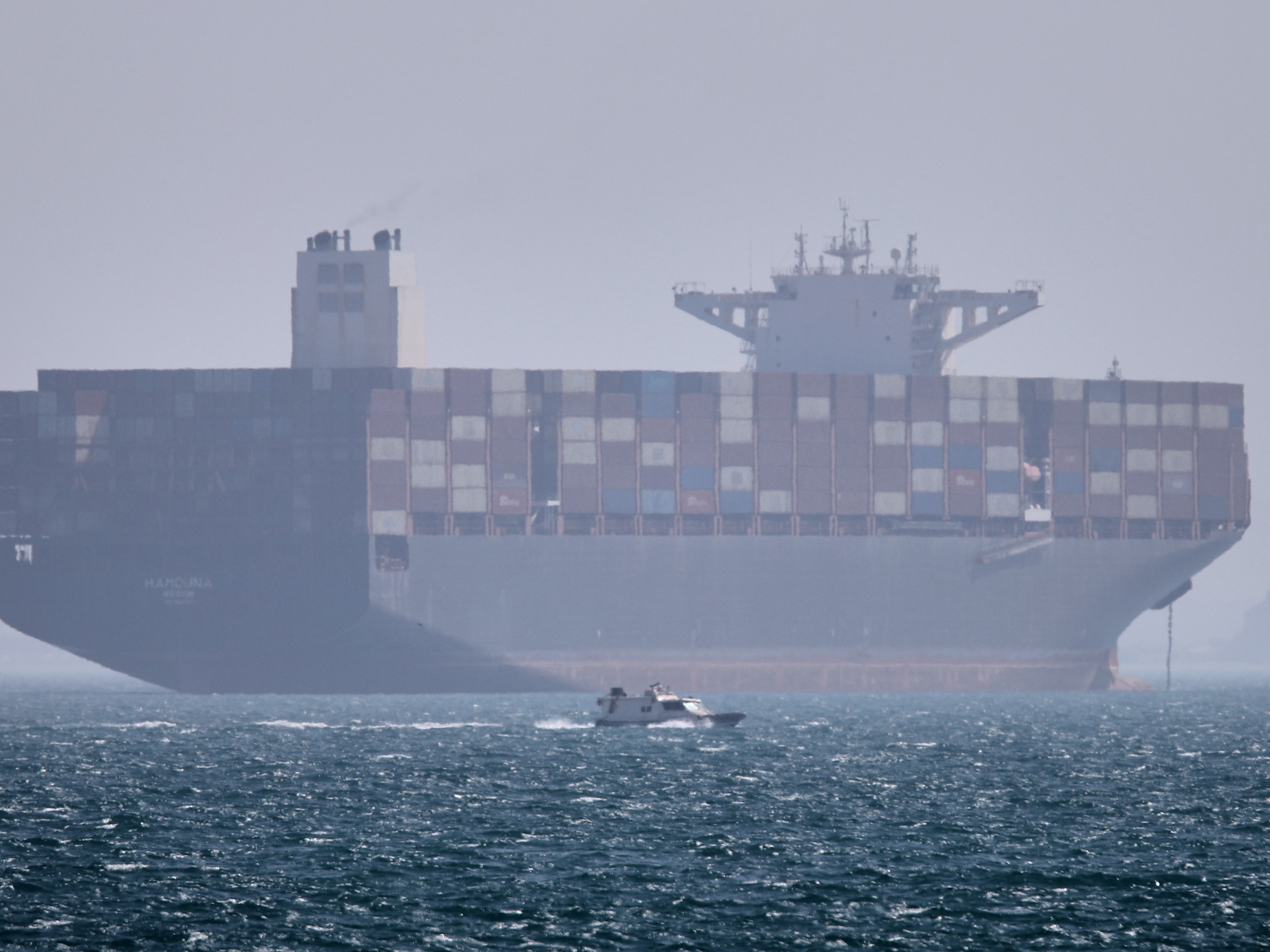 caption: A container ship sits at anchor as a small motorboat passes in the foreground in the Strait of Hormuz off Bandar Abbas, Iran, on May 2.