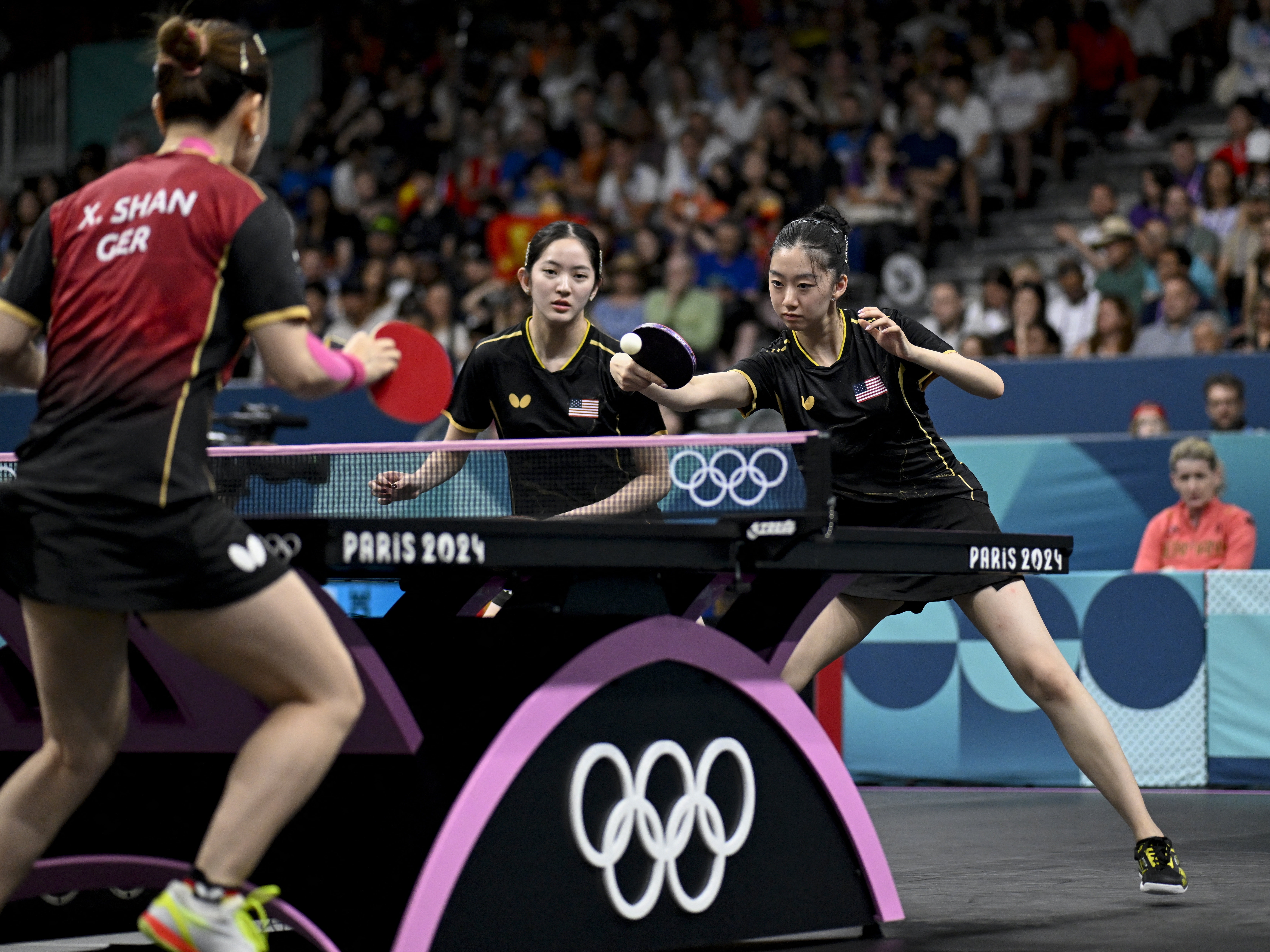 caption: Rachel Sung and Amy Wang of the U.S. women's table tennis team take on Germany during the 2024 Olympic Games in Paris. 