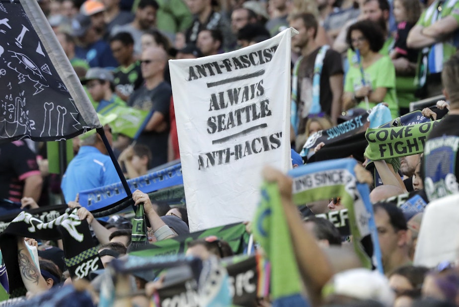 caption: In this July 21, 2019, photo, a sign that reads "Anti-Facist Always Seattle Anti-Racist" is displayed in the supporters section during an MLS soccer match between the Seattle Sounders and the Portland Timbers in Seattle. 