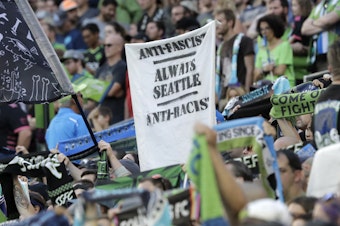 caption: In this July 21, 2019, photo, a sign that reads "Anti-Facist Always Seattle Anti-Racist" is displayed in the supporters section during an MLS soccer match between the Seattle Sounders and the Portland Timbers in Seattle. 