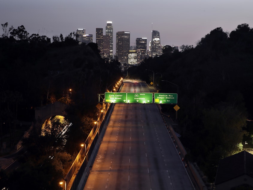 caption: California State Route 110 seen with downtown Los Angeles in the background Thursday night. The state is in its second week of a lockdown, where schools and nonessential businesses are closed and the governor has ordered people to stay home.
