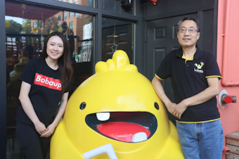 caption: Michelle Liu and her father Chuan Liu pose with their store's mascot as they celebrate the upgrades to their store, Boba Up, in Seattle's University District. 