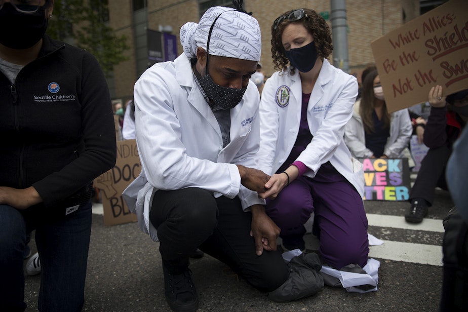 caption: A tear falls from Dr. Hayden Hamilton's eye while kneeling with Dr. Jennifer Hamilton, right, during a moment of silence on Saturday, June 6, 2020, outside of Harborview Medical Center in Seattle. Thousands of nurses, doctors, and health care workers came together to protest police violence with a march to Seattle City Hall. "We need to think of racism as a disease,” said Organizer Dr. Estell Williams, a general surgeon at the University of Washington. 