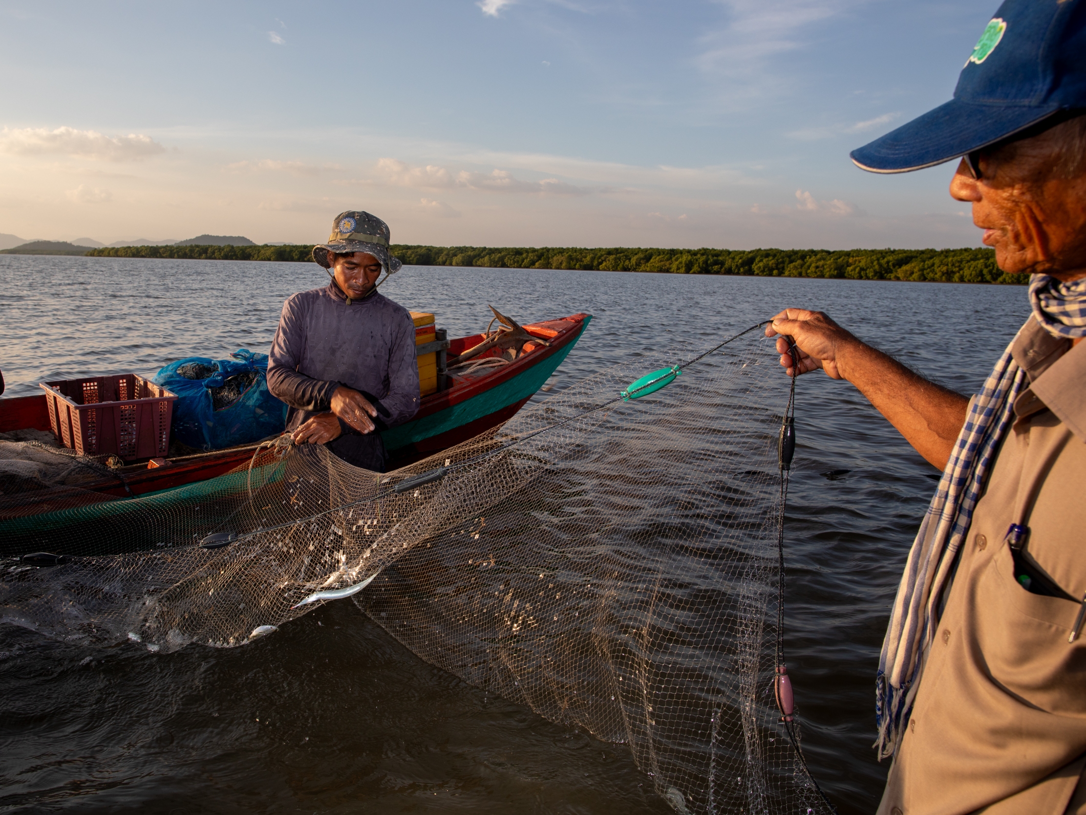 caption: Local fisheries on the coast of Cambodia struggled with decimated fish populations for years. Today, they are teeming with seafood, thanks to local ecological restoration efforts. Here (at right), Koh Kresna village chief Khiev Sat talks with a fisherman about the day's catch.