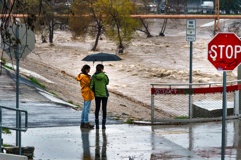caption: People watch the high volume of storm rain water flowing downstream at the Los Angeles River in Los Angeles on Saturday, Jan. 14, 2023. Storm-battered California got more wind, rain and snow on Saturday, raising flooding concerns, causing power outages and making travel dangerous. 