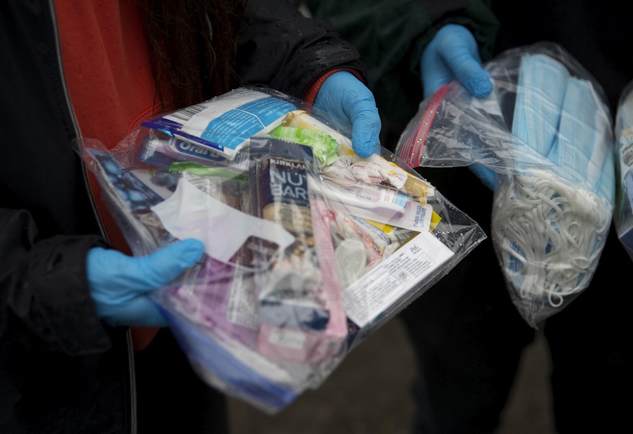 caption: Joscelyn and Cass DuVani hold bags packed with masks,  snacks, toothbrushes, tampons, candy, and several other items to deliver to unhoused community members on Friday, March 5, 2021, near the intersection of 10th Avenue South and South Dearborn Street in Seattle. 