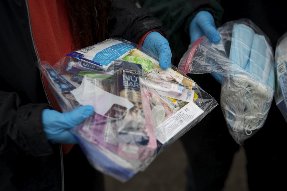 caption: Joscelyn and Cass DuVani hold bags packed with masks,  snacks, toothbrushes, tampons, candy, and several other items to deliver to unhoused community members on Friday, March 5, 2021, near the intersection of 10th Avenue South and South Dearborn Street in Seattle. 
