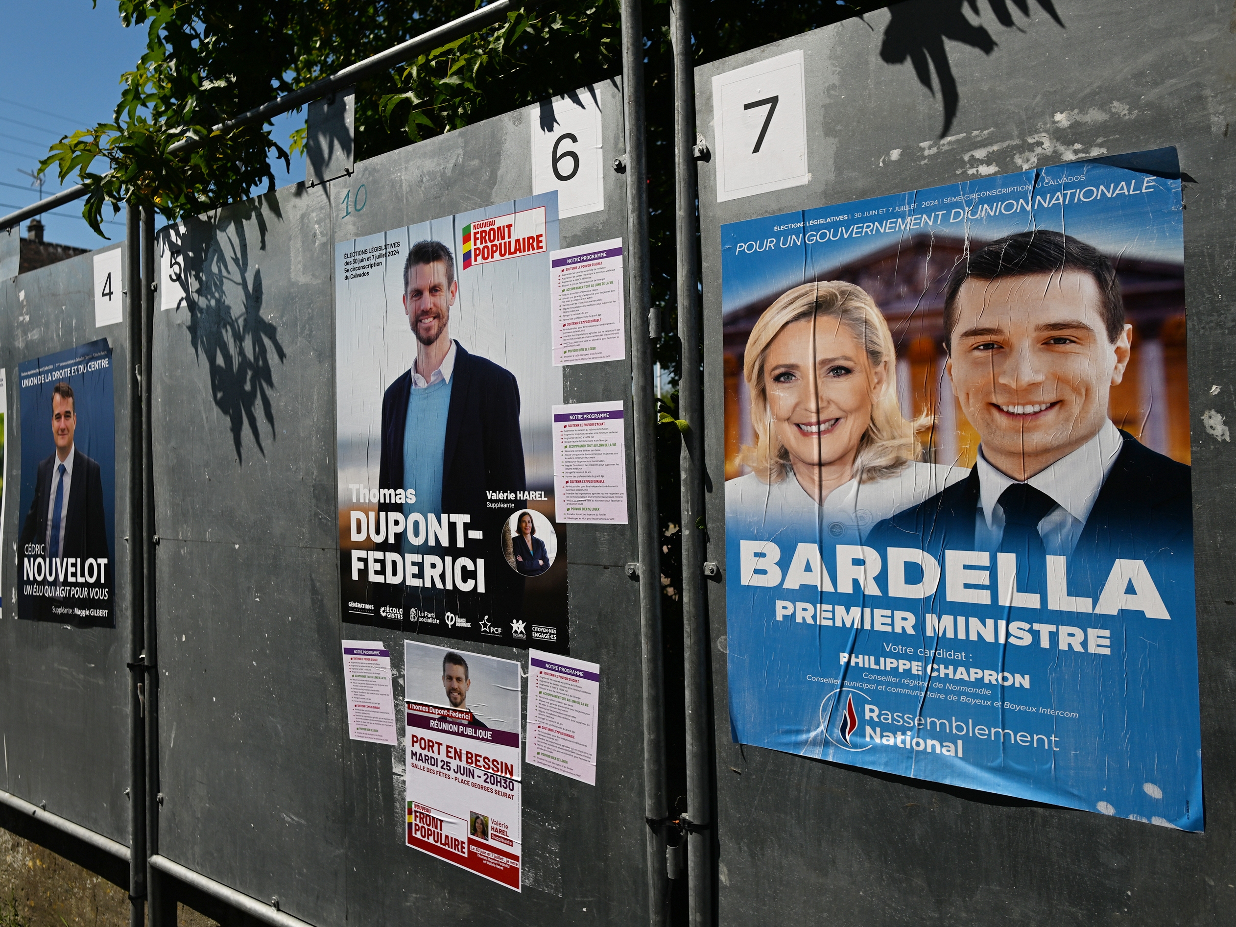 caption: Posters with images or names of local candidates for the first round of the 2024 French legislative elections displayed in front of the local town hall in Port-en-Bessin-Huppain, Normandy, France, on June 25. France will hold an early legislative election in two rounds, on June 30 and July 7.