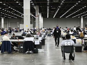 caption: Ballot counters process absentee ballots on Nov. 8 at Huntington Place in Detroit. The scene this year was much calmer than 2020, when protesters descended on Detroit and yelled for election officials to "stop the count!"