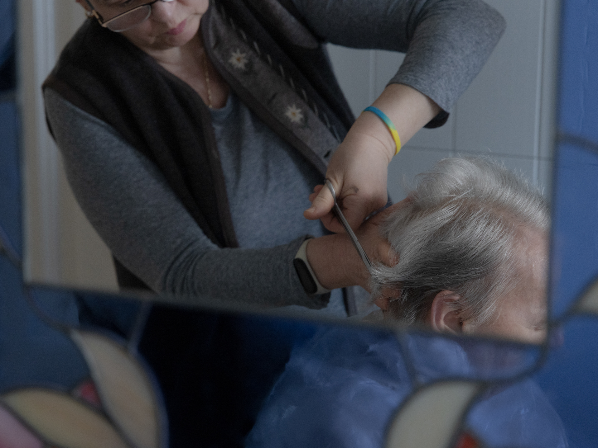 caption: Caregiver Liliya Khodunay cuts Anna's hair in Anna's home in Milan, Italy, in February 2023.