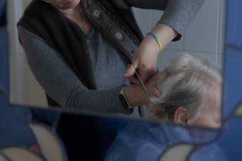 caption: Caregiver Liliya Khodunay cuts Anna's hair in Anna's home in Milan, Italy, in February 2023.
