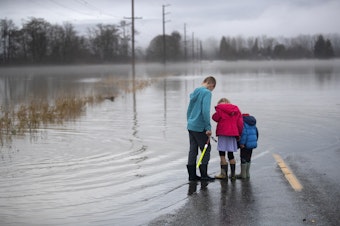 caption: From left, Noah Enter, 8, Ainsley Enter, 5, and Lucas Enter, 2, listen to noises made by flood water bubbling up through the roadways cracks, on Wednesday, December 6, 2023, along Francis Road in Clear Lake. 