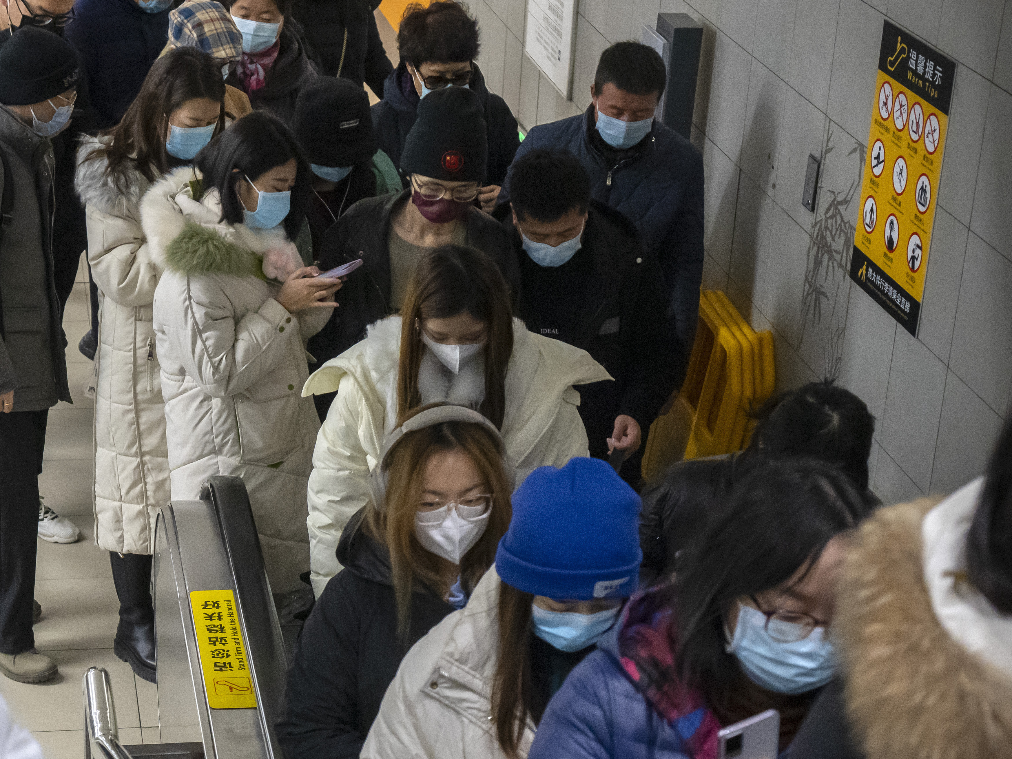 caption: Commuters wearing face masks  ride an escalator at a subway station in the central business district in Beijing. Caseloads of omicron have remained relatively low in many parts in Asia.