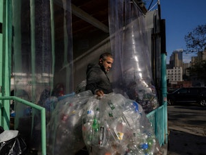 caption: A worker carries used drink bottles and cans for recycling at a collection point in Brooklyn, New York. Three decades of recycling have so far failed to reduce what we throw away, especially plastics.