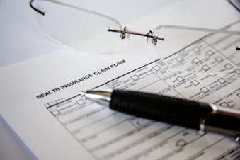 caption: A zoomed in photograph of a health insurance claim form next to glasses and a pen.