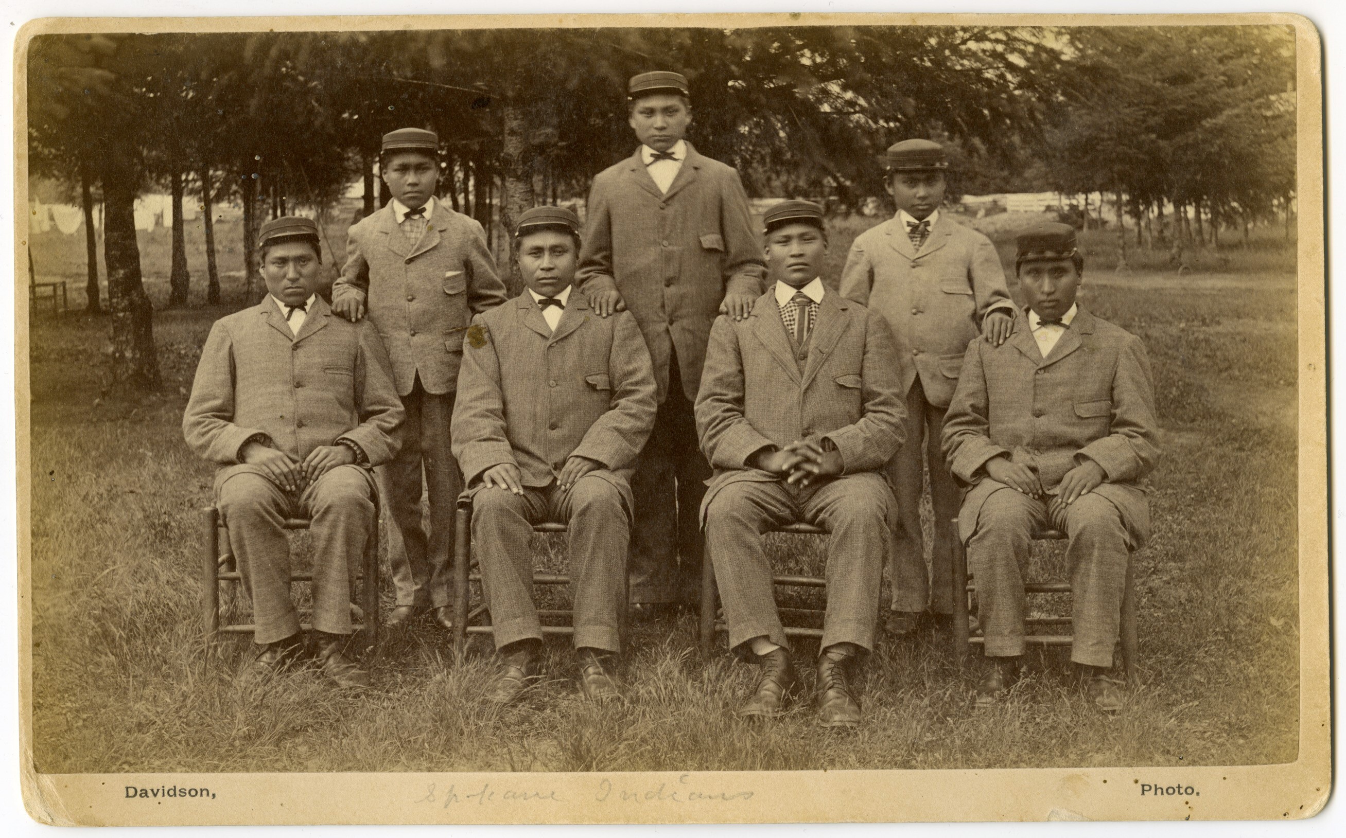 caption:  This historical photo, provided to Oregon Public Broadcasting by Pacific University archivist Eva Guggemos, shows seven boys who came to the Forest Grove Indian Training School from the Spokane tribe in 1880. The Forest Grove school operated for a few years before being relocated to Salem and renamed Chemawa Indian School.