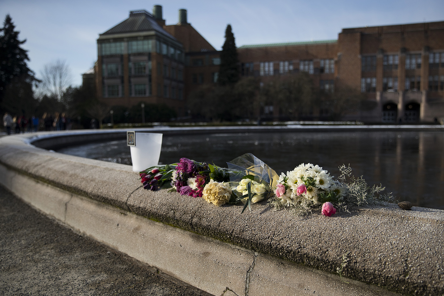 caption: Flowers are placed on the edge of the Drumheller Fountain on Thursday, February 7, 2019, on the University of Washington campus in Seattle. A 19-year-old student died on Wednesday morning after slipping and falling. 