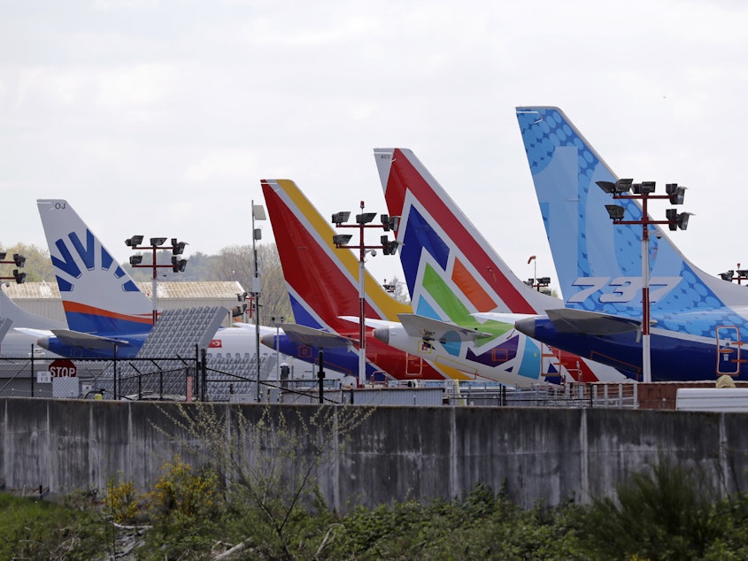 caption: A line of Boeing 737 MAX jets sit parked on the airfield adjacent to a Boeing production plant last month in Renton, Wash. Boeing now says it is cutting thousands of jobs.