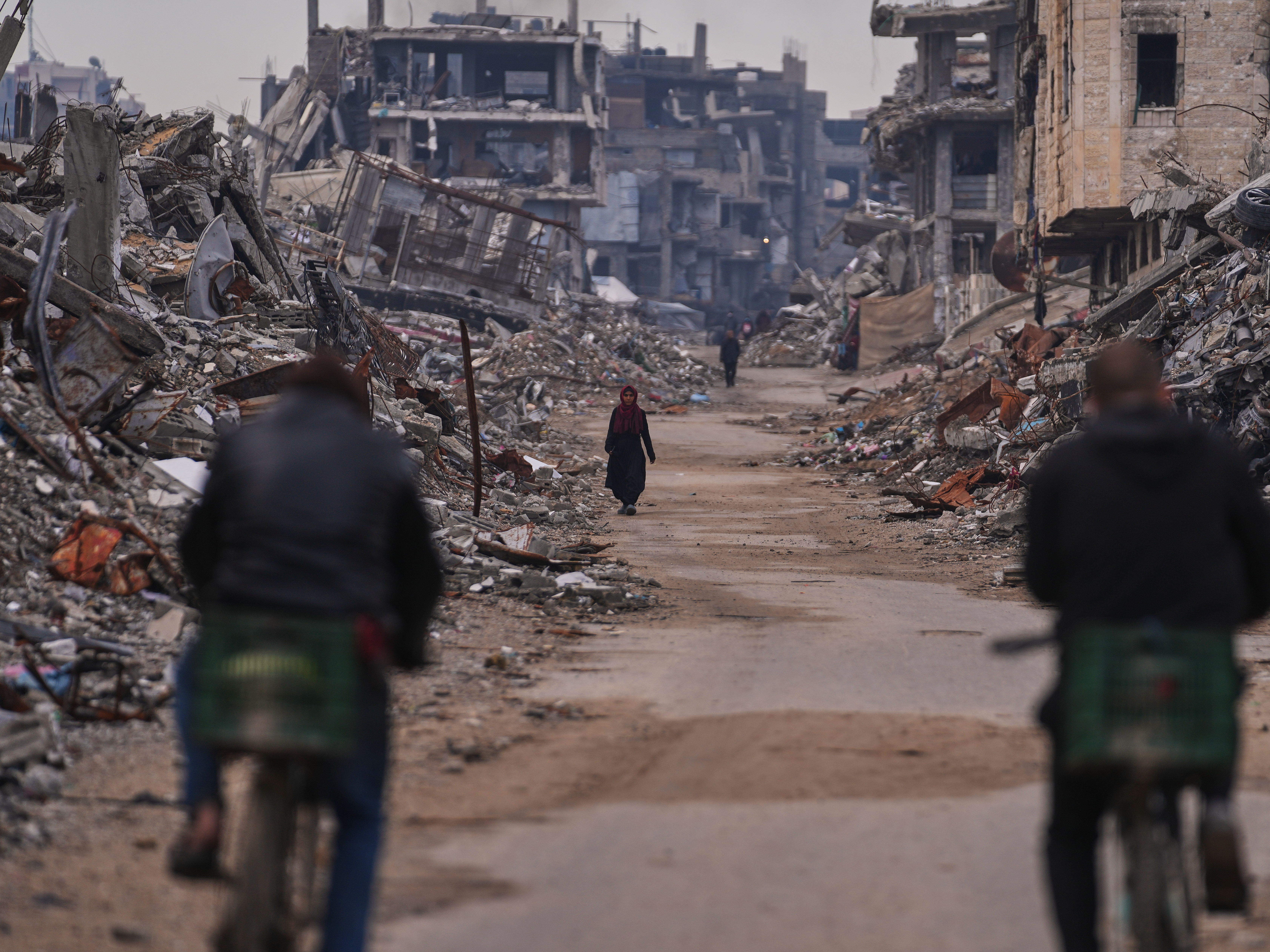 caption: A Palestinian woman walks along a street surrounded by buildings destroyed during Israeli air and ground operations in the Sheikh Radwan neighborhood, in Gaza City, Tuesday.