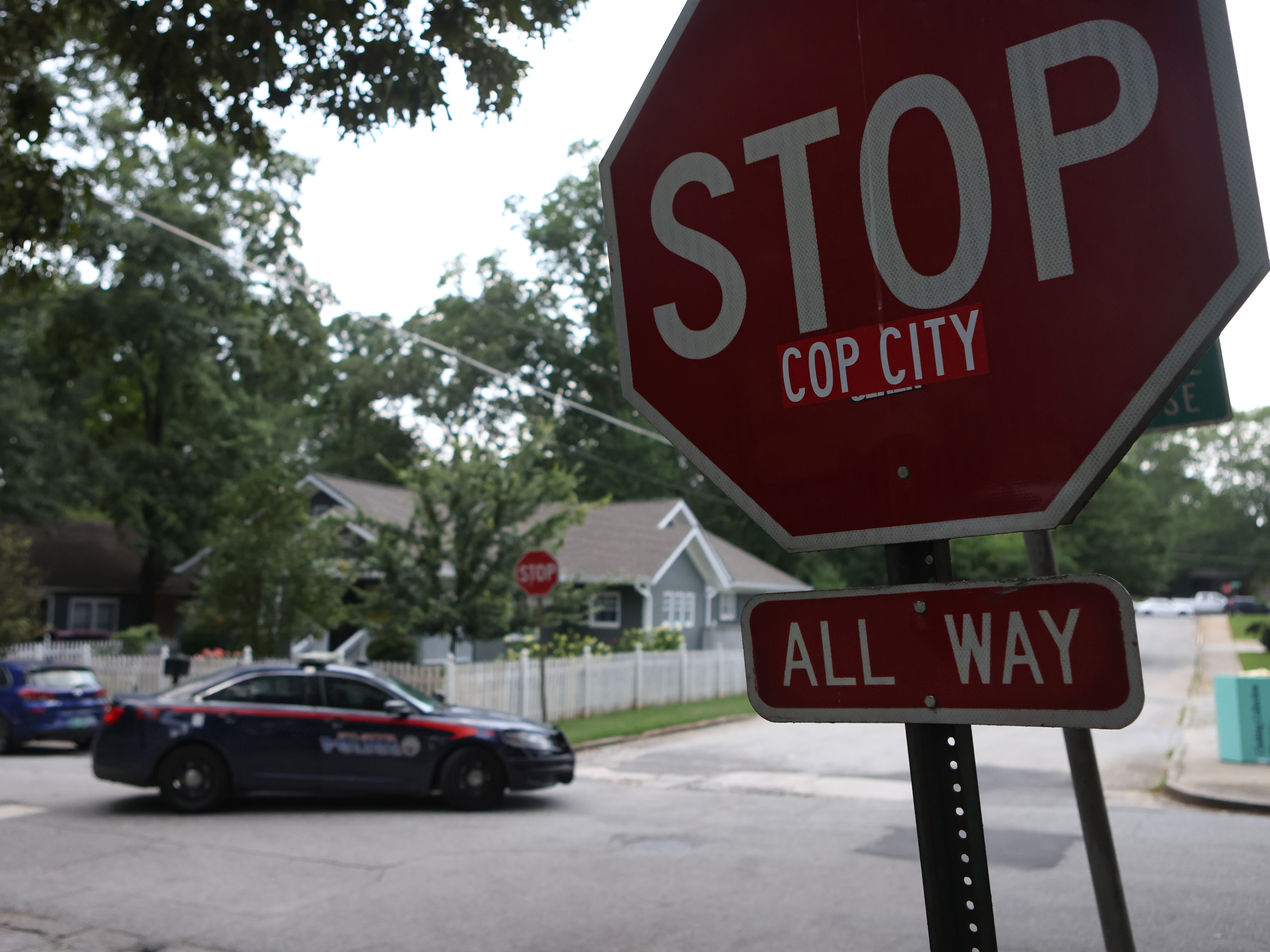 caption: A police car drives through an intersection near Brownwood Park on Saturday where a stop sign has been modified in opposition to the Atlanta Public Safety Training Center that protesters refer to as "Cop City," in Atlanta.