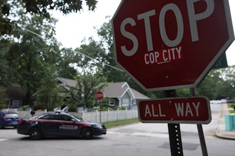 caption: A police car drives through an intersection near Brownwood Park on Saturday where a stop sign has been modified in opposition to the Atlanta Public Safety Training Center that protesters refer to as "Cop City," in Atlanta.