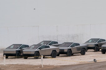 caption: Newly manufactured Tesla Cybertrucks are parked outside the company's Giga Texas factory on December 13, 2023, in Austin, Texas.