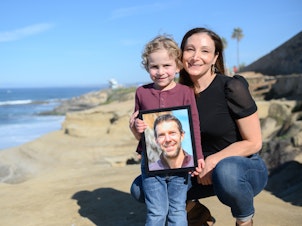 caption: Laura Keenan and her son, Evan, hold a photo of her late husband Matt Keenan, who was killed while riding his bike in San Diego in 2021.
