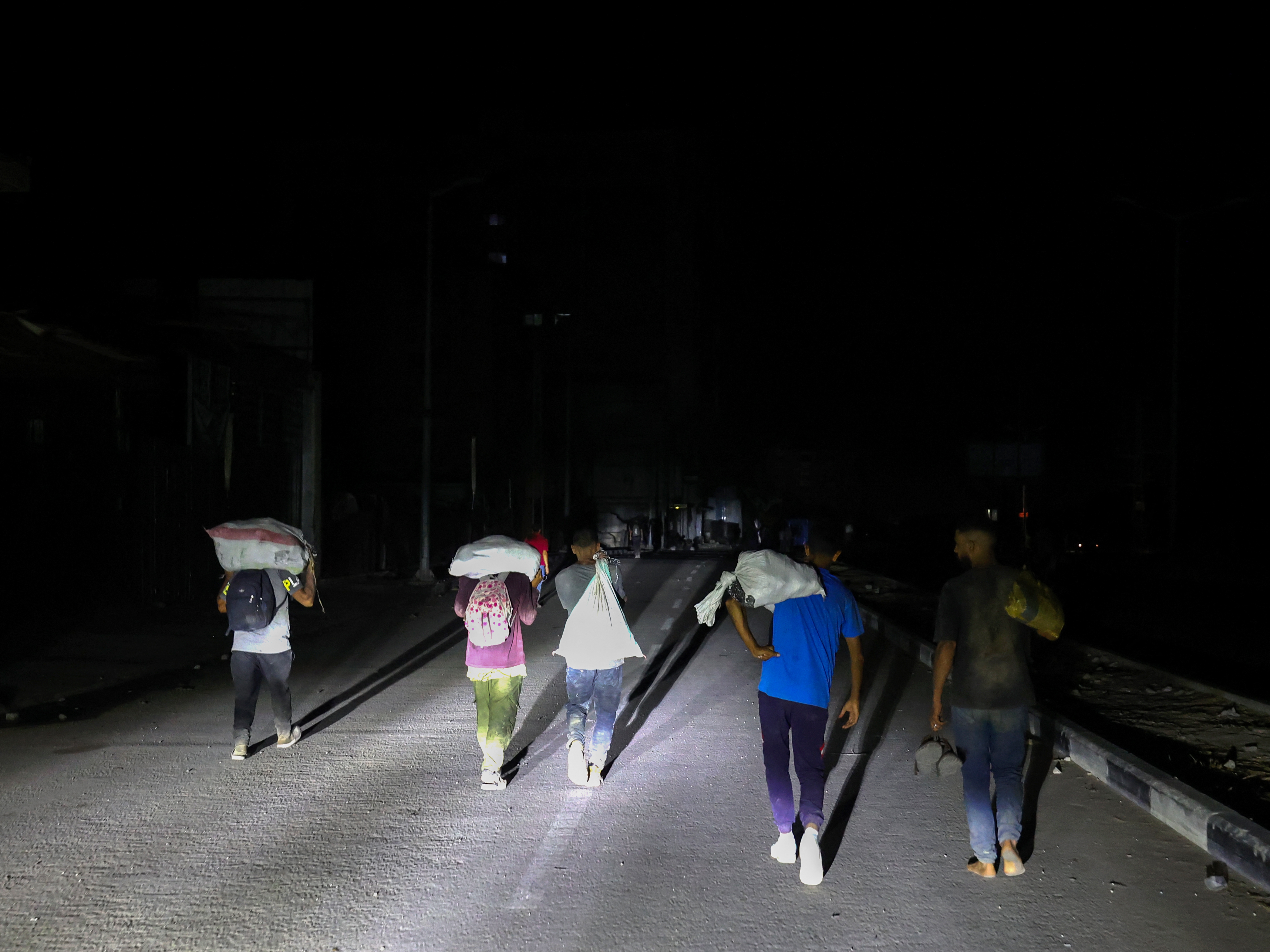 caption: Palestinians walk back, carrying parcels collected from a food aid distribution point set up by the privately run Gaza Humanitarian Foundation (GHF) on the Salaheddin road, at the Nuseirat refugee camp in the central Gaza Strip on June 24, 2025.
