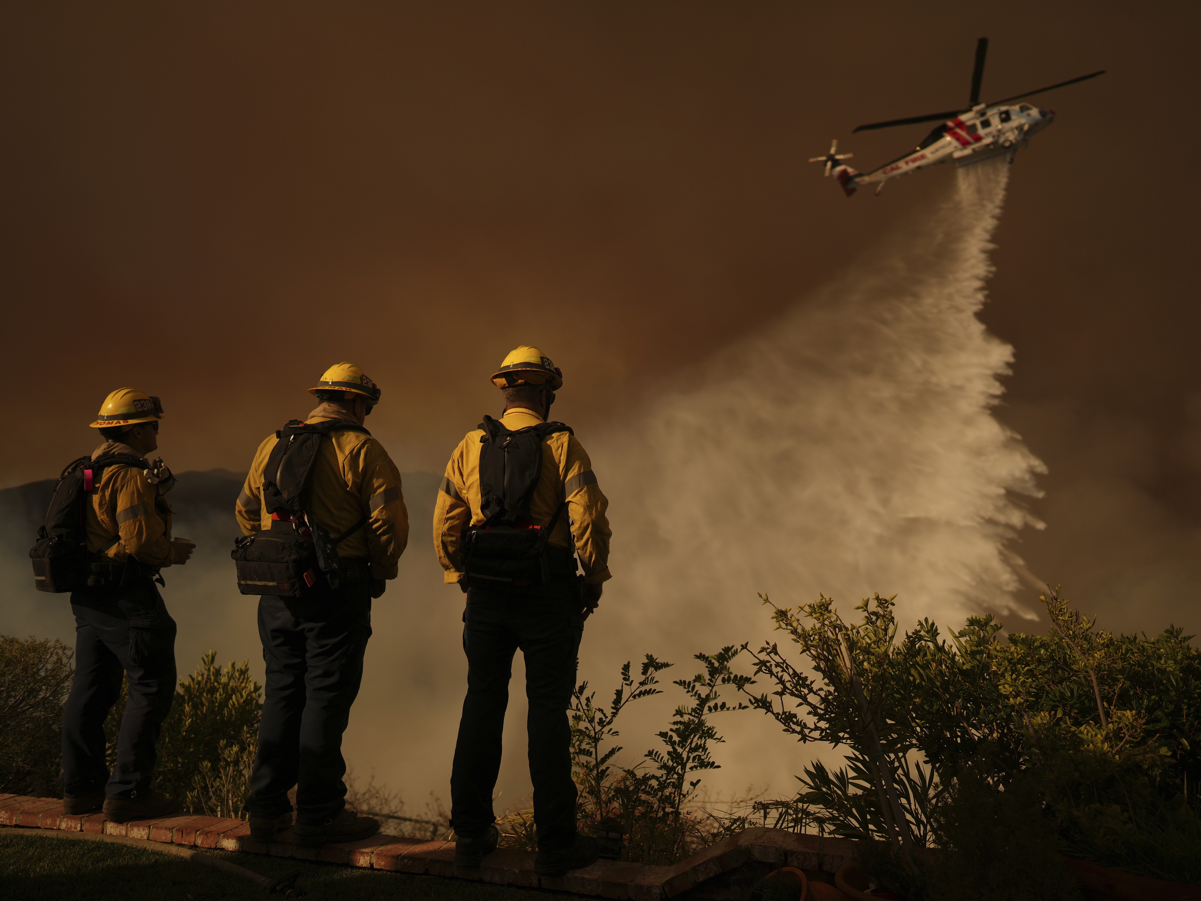 caption: A helicopter drops water on Mandeville Canyon as the Palisades Fire rages Saturday in Los Angeles.