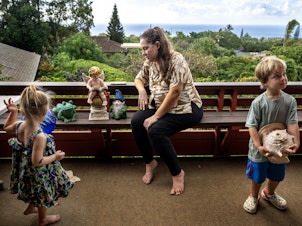 caption: Arica Lynn Souza and her children Ayla, 3, left, and Silas, 4, on the porch of the family home where they are staying temporarily after losing their Lahaina townhome in the wildfires.