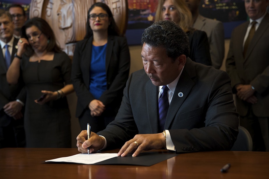 caption: Seattle City Council President Bruce Harrell signs an executive order on Wednesday, September 13, 2017, after taking the oath of office and becoming the mayor of Seattle at City Hall.