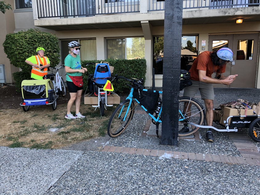 caption: From left, bike volunteers Janine Jordan, Ellen Nichter, and David Urbina prepare to deliver boxes of food and produce to families at this White Center apartment building.